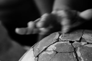 A close-up image of a roman pot. The blur of a hand tending to a crack in the structure is depicted. This image is in black and white.