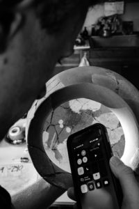 Ένας άνδρας δείχνει έναν φακό τηλεφώνου στο εσωτερικό ενός ρωμαϊκού δοχείου. Αυτή είναι μια ασπρόμαυρη εικόνα.