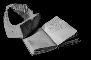 The remains of an object weighed on a field journal, holding the page open to a handwritten entry. This image is in black and white.