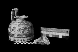 An oiochoe (wine jar) featured on the left, with a measurement tool placed in front of it. A Kodak color control strip sits on the right. The image is in black and white.