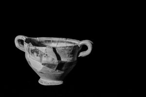 A small pot with a large piece of the side broken off but reapplied with a piece of tape. This image is in black and white.