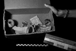 A cardboard box full of loose and broken artifacts being held up to see. The Kodak color patch sheet peeks out from the bottom of the photo. This image is in black and white.